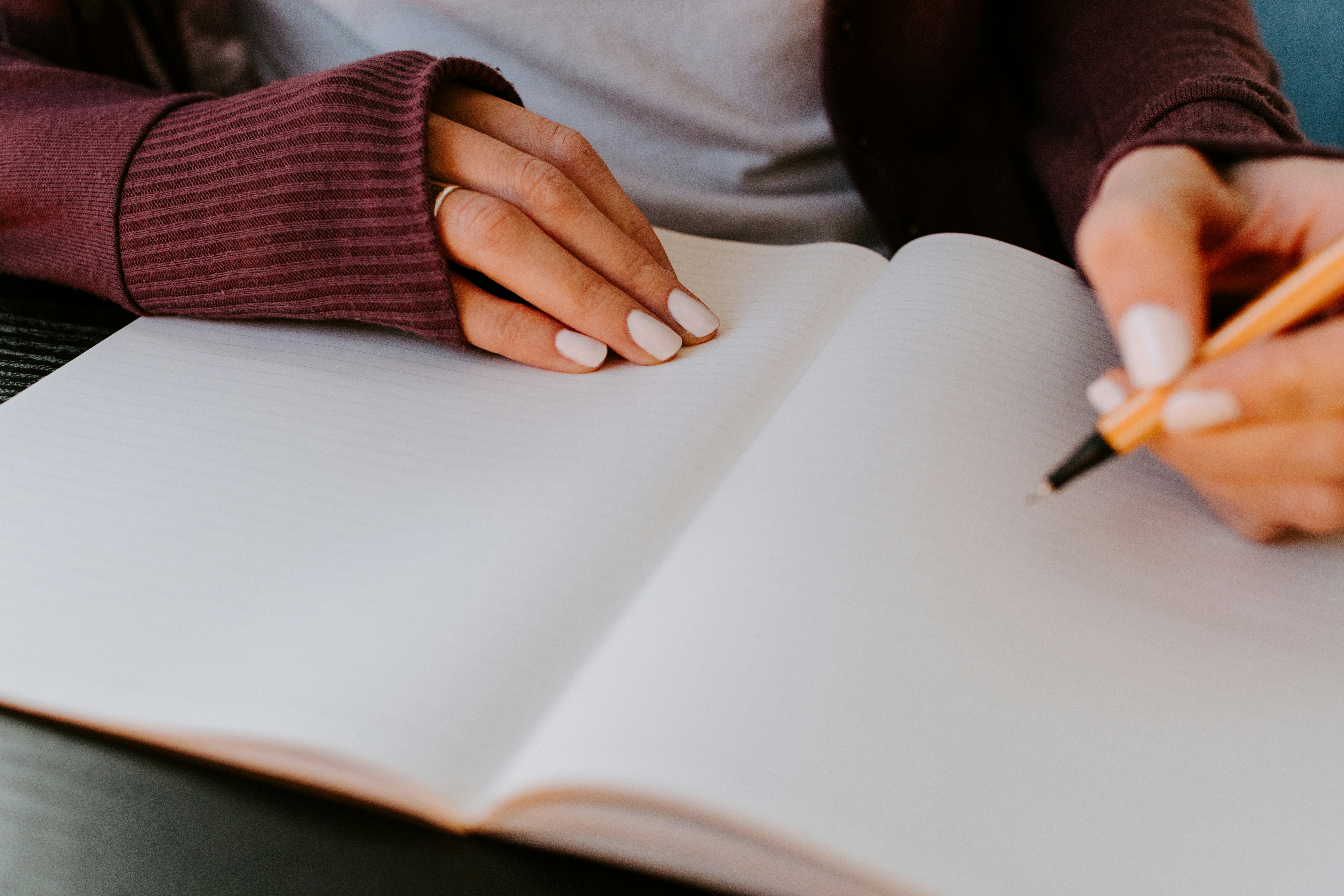 open notebook with someone's right hand holding the pages down and left and holding a pen getting ready to write