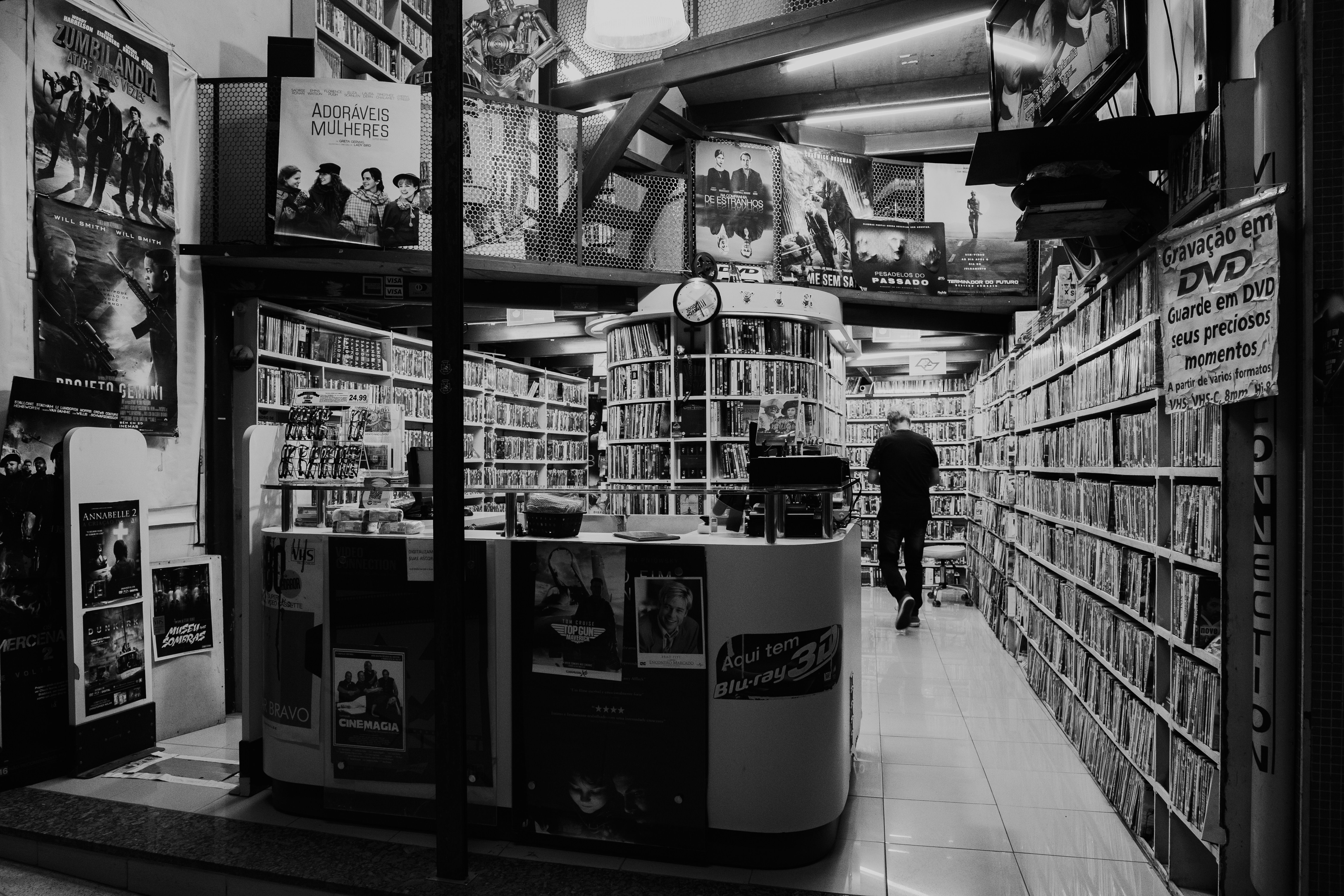 Website logo of shelves to the ceiling full of DVDs in a shop with posters and a lone customer in black and white